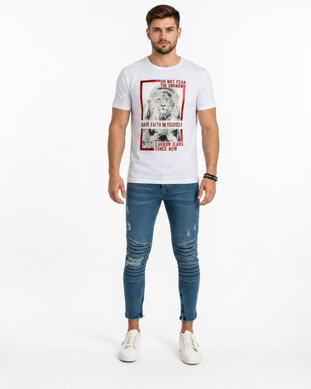 A man stands wearing a white graphic t-shirt featuring a lion design, paired with distressed blue jeans and white sne...