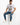A man sits on a white cube, wearing a graphic t-shirt and distressed skinny jeans, paired with white sneakers.