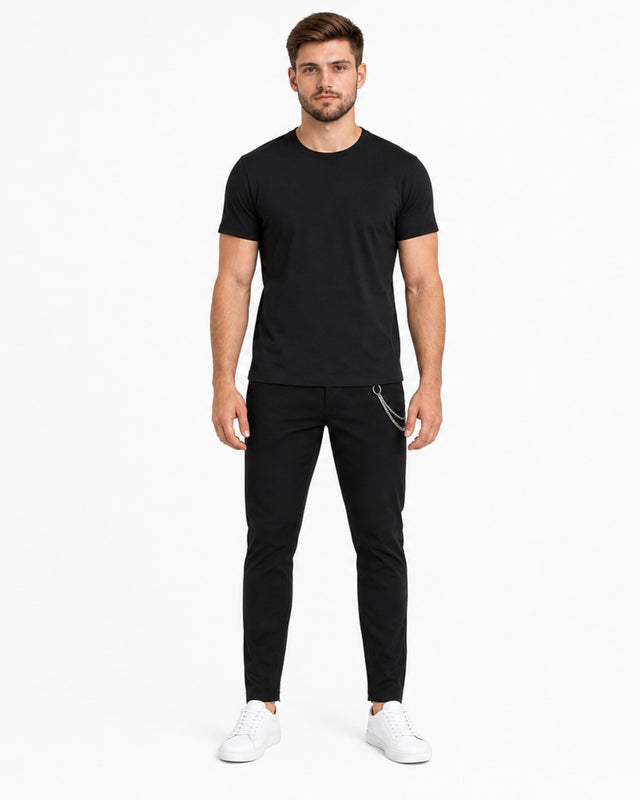 A man stands confidently in a fitted black t-shirt and slim black pants, paired with white sneakers.