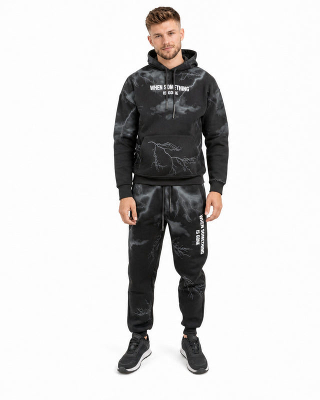 A man wearing a black hoodie and matching sweatpants with a lightning design and graphic text.