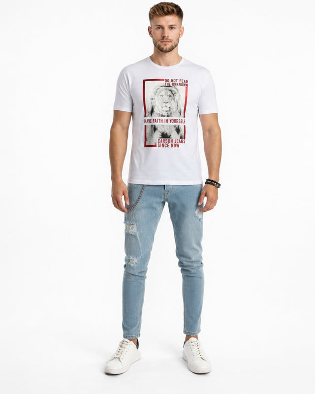 A man stands wearing a white graphic t-shirt and light blue distressed jeans, paired with white sneakers.