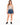 A woman stands wearing a tie-dye tank top and denim shorts, paired with black sneakers against a white background.