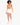 A model with curly hair wears an orange bodysuit and white shorts, walking in white sneakers against a light background.