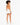A model with curly hair wearing an orange bodysuit and white shorts, standing with her back to the camera.