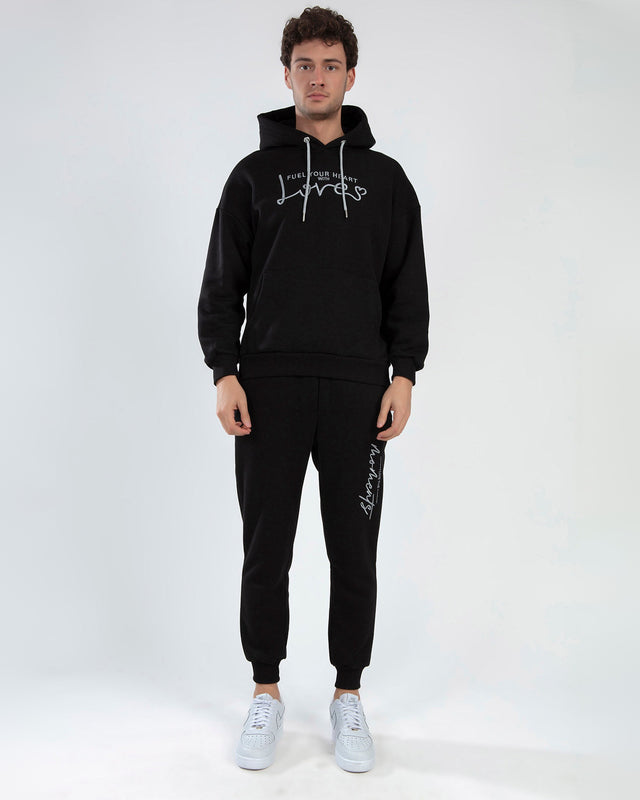 Live The Moment black streetwear pants with white graphic text on left leg, paired with matching hoodie.
