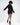 A model showcases a black oversized hoodie dress with a unique hemline and side slits, paired with stylish black ankl...