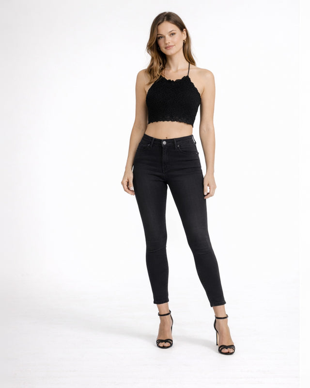 A model poses in a black lace crop top and fitted black jeans, paired with strappy black heels.