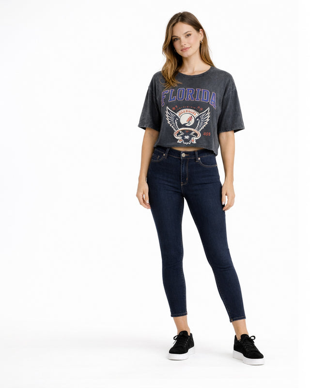 A woman stands confidently in a cropped graphic tee featuring a Florida design, paired with dark skinny jeans and bla...