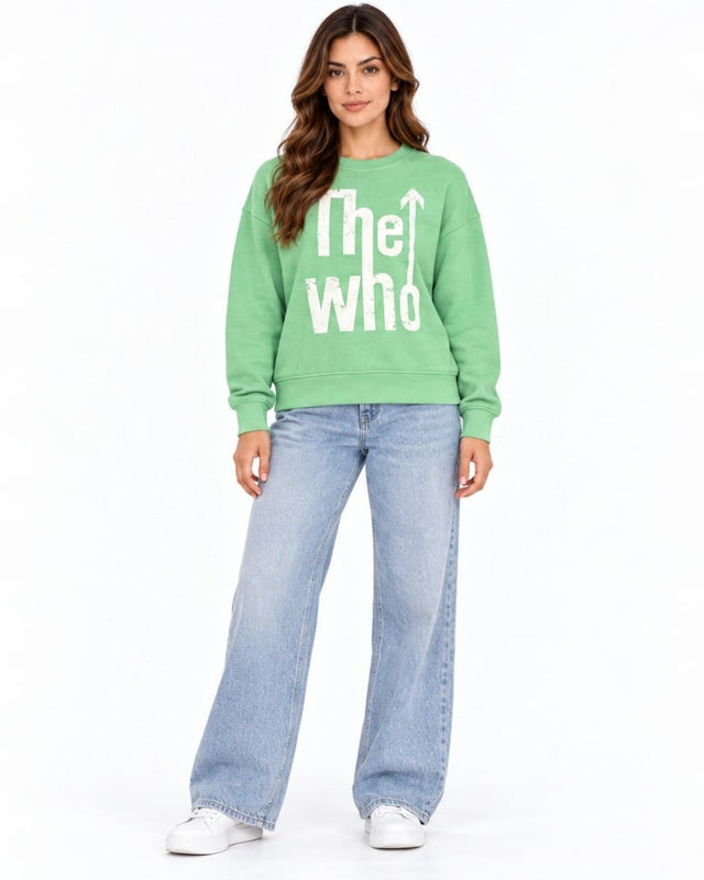 A woman stands wearing a green sweatshirt with white text, paired with light blue wide-leg jeans and white sneakers.