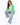 A woman sits on a stool wearing a green sweatshirt with bold white lettering, paired with light blue jeans and white...