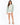 A woman stands wearing a light green sweatshirt with bold cream text, paired with white shorts and beige heels.