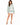 A woman stands wearing a light green sweatshirt with bold white lettering, paired with a white skirt and heels.