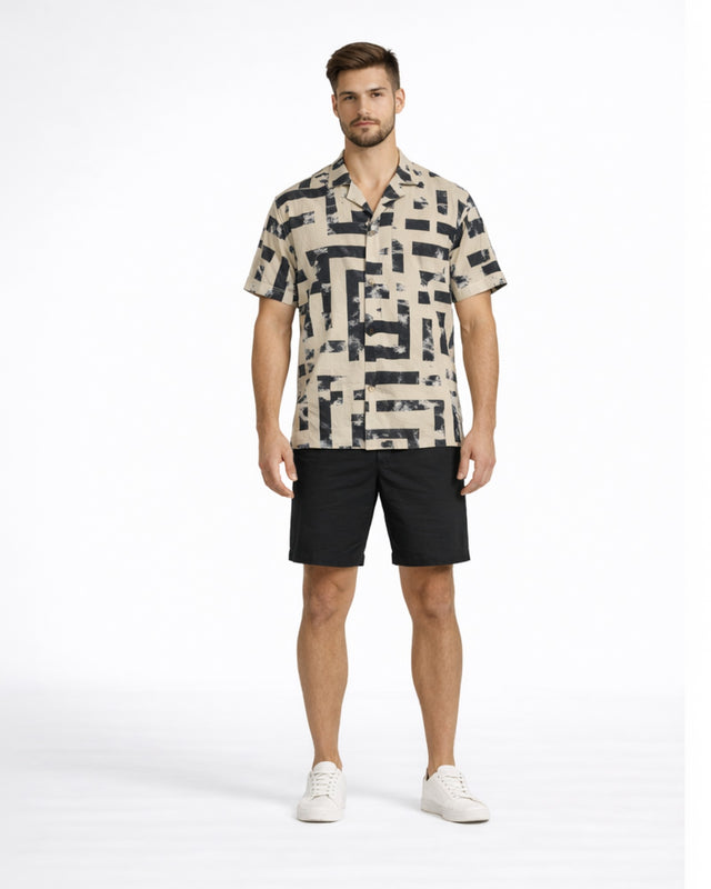 A man stands confidently in a patterned short-sleeve shirt and black shorts, paired with white sneakers.