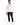 A man wearing a long-sleeve white shirt with a circular graphic and text, paired with black ripped jeans and white sn...