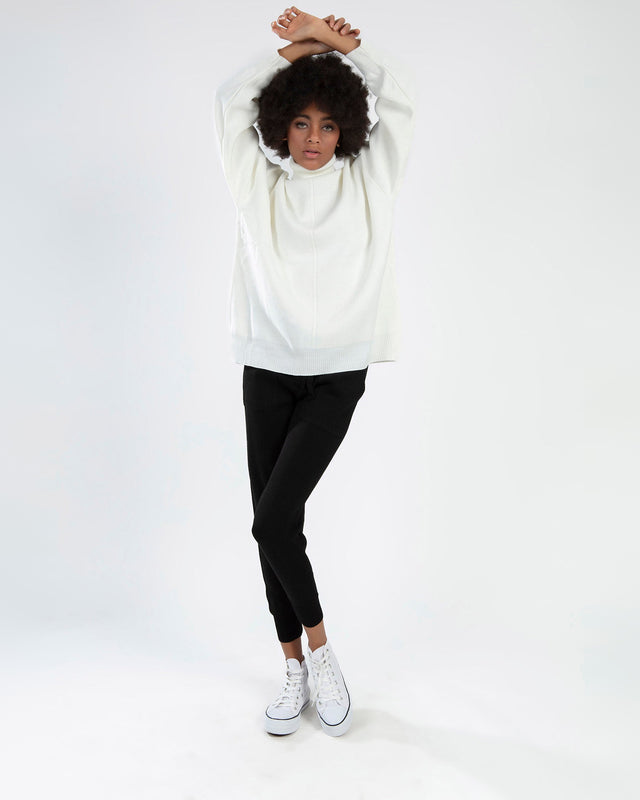 Model wearing the Mabel cream knit sweater, a white oversized turtleneck, paired with black leggings and white sneakers.