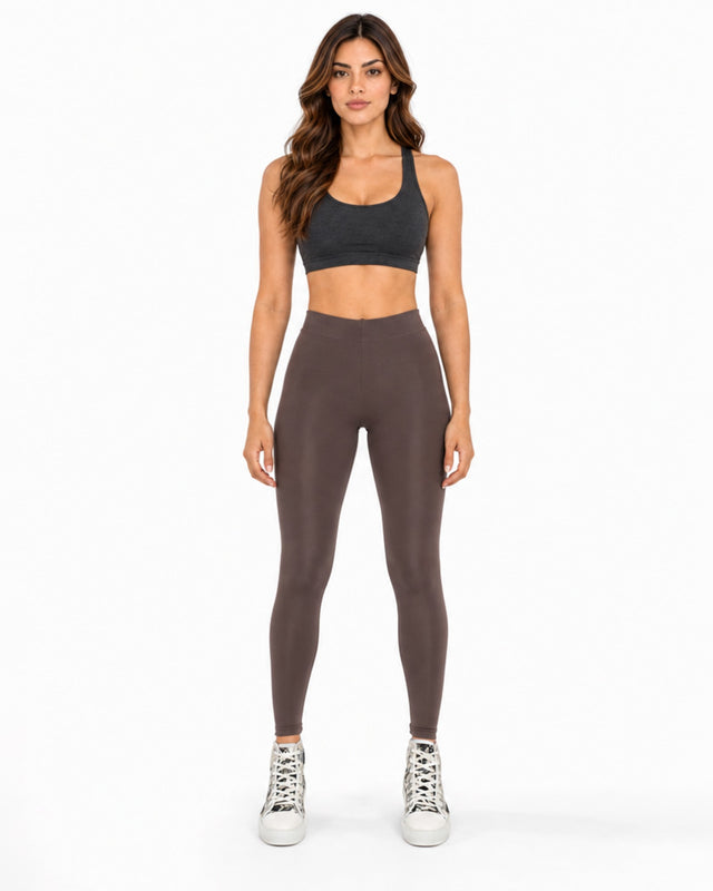 A woman stands confidently in fitted brown leggings paired with a dark sports bra and stylish sneakers.