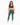 A woman stands confidently in fitted green leggings and a dark sports bra, paired with white sneakers.