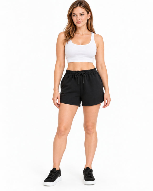 Woman in black drawstring sweat shorts and a white crop top with black sneakers, front view