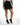 Maddison black high-waisted mini skirt featuring an asymmetrical wrap front and eyelash lace trim at the hem.