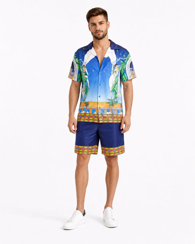 A man stands wearing a colorful short-sleeve shirt with a tropical design and matching shorts, paired with white snea...