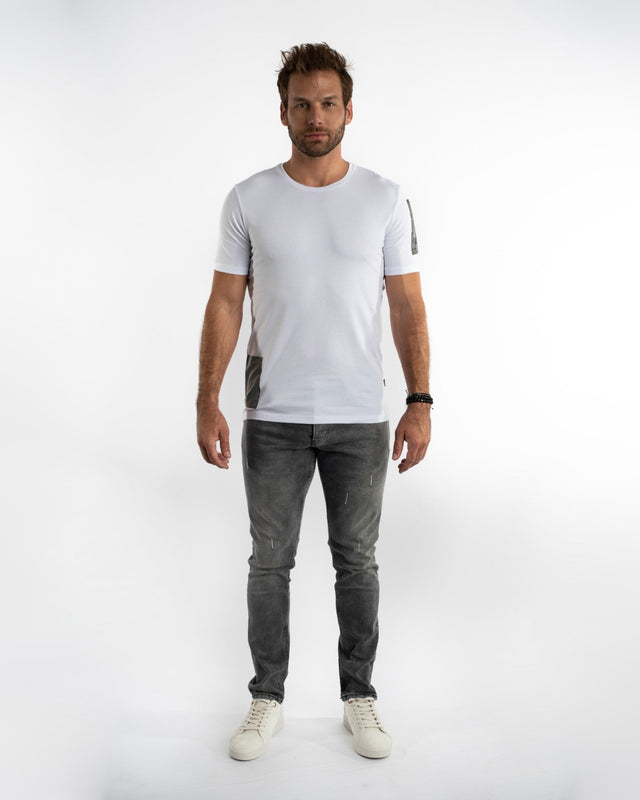 A man stands confidently in a fitted white t-shirt and gray jeans, complemented by white sneakers.