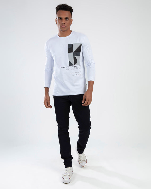 Man wearing Marcus dark blue jeans with a long-sleeved graphic white t-shirt and white sneakers.