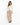 A woman in a fitted cream jacket paired with beige trousers and black heeled sandals, standing against a white backgr...