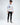 A young man stands in a white long-sleeve shirt with colorful graphics, paired with black ripped jeans and sneakers.