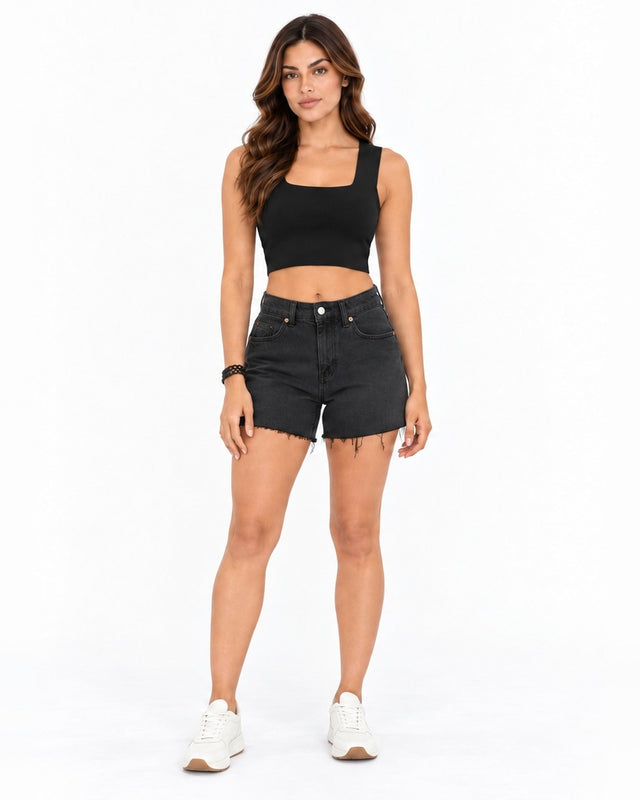 A model poses in a fitted black crop top and distressed black shorts, paired with white sneakers.