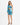 A model poses in a vibrant blue and green one-shoulder dress with a cutout and ruched detailing.