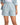 Light blue pleated shorts with rolled cuffs and side pockets, styled for a casual yet polished look.