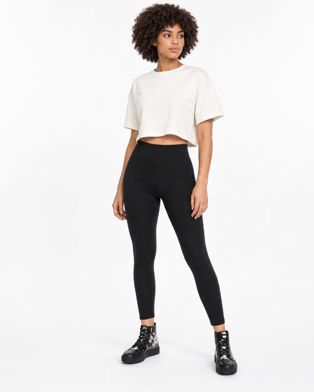 A model wearing black leggings paired with a cropped white t-shirt and stylish black boots.