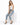 A woman sits on a white pedestal wearing light blue distressed jeans and a fitted white tank top with black heels.