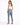A woman stands with her back to the camera, wearing light blue jeans and a white tank top, paired with black heels.