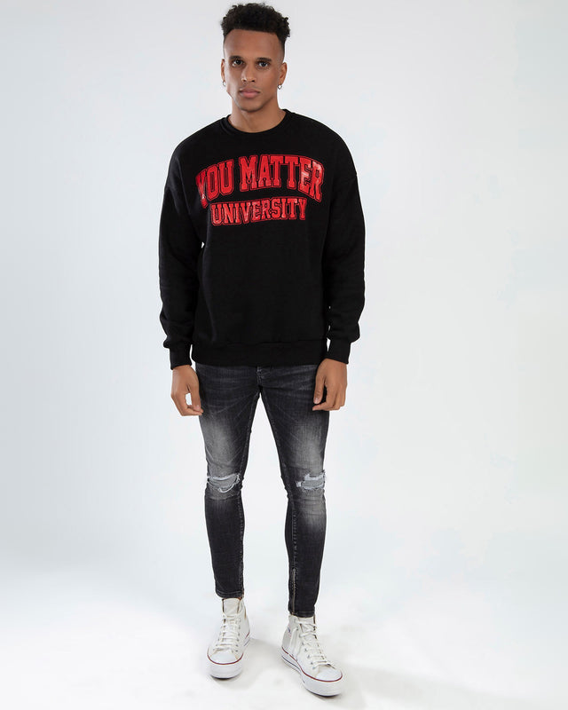 Model wearing black You Matter University graphic sweatshirt and distressed gray skinny jeans.
