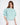 Model in teal More and Less cropped sweatshirt with embossed text and puff sleeves against a white background.