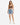A woman stands confidently in a fitted brown crop top paired with distressed denim shorts and white sneakers.