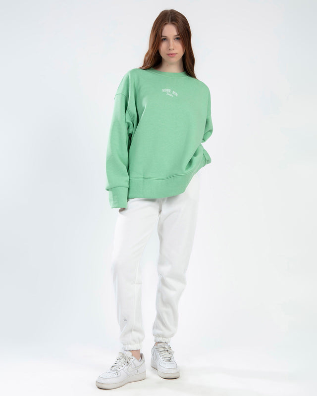 Model in Eve mint green oversized sweatshirt with More and Less graphic, paired with white sweatpants.
