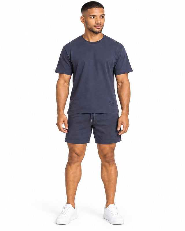 A man stands confidently in a navy blue short-sleeve top paired with matching shorts and white sneakers.