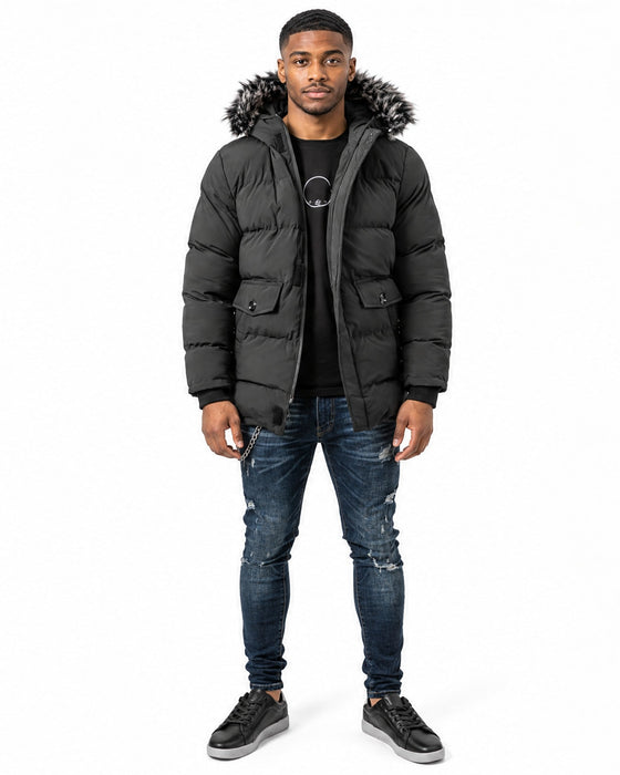 A man stands wearing a black puffer coat with a fur-lined hood, paired with a black t-shirt and distressed jeans.