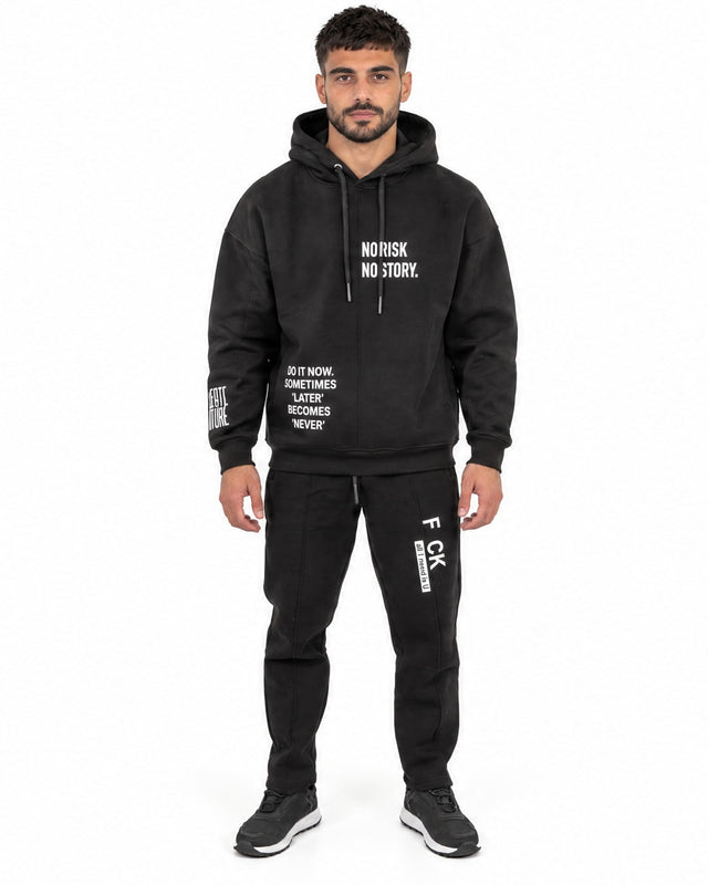 A man wearing a black hoodie with motivational text and matching black joggers, standing confidently.