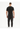 A man wearing a black t-shirt and dark pants stands with his back to the camera, showcasing a casual outfit.