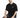 A man sits on a white pedestal wearing a black oversized t-shirt and distressed jeans, showcasing a casual style.