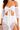 A model wears a white off-the-shoulder top with sheer puff sleeves and a matching wrap skirt.