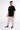 Man wearing black Survive Graphic T-Shirt with white text, paired with tan cargo joggers and black sneakers.