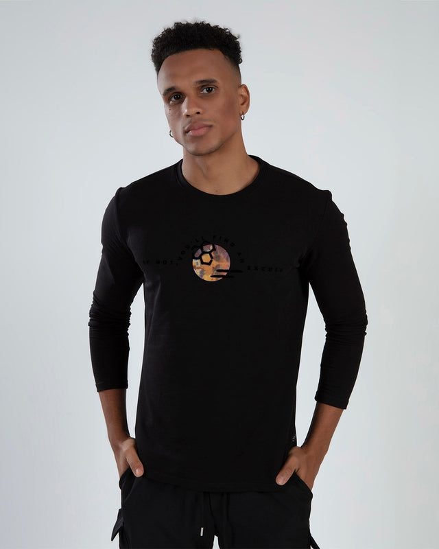 A young man poses in a black long-sleeve shirt featuring a colorful graphic design on the front.