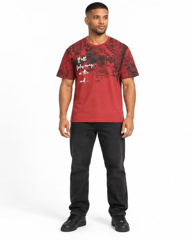A man stands wearing a red graphic t-shirt with a black abstract design and white text on the front.