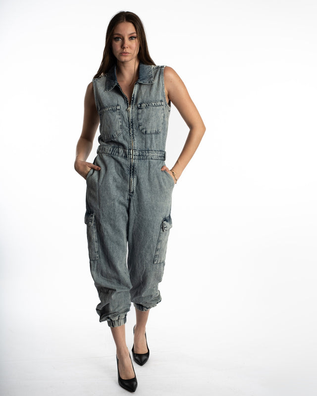 Model wearing a Faye blue acid wash denim utility jumpsuit with cargo pockets, zip-front, and tapered jogger cuffs.