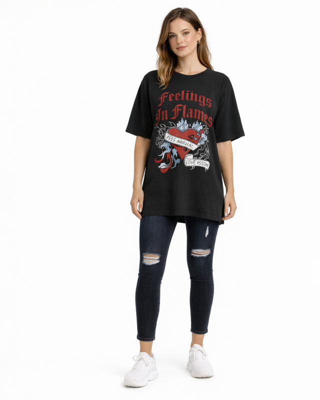 A model wearing a black oversized tee with a graphic design featuring a heart and flames, paired with ripped jeans an...