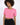 A model wearing a cropped pink top with short sleeves and two front pockets, paired with black pants.